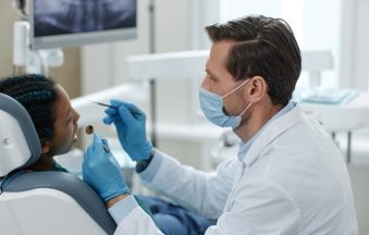 Side view portrait of male dentist wearing mask while working with child patient in clinic